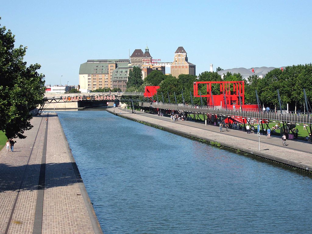 The Canal de l'Ourcq, in the background the Grands Moulins de Pantin and on the right the inflatable roof of the Zénith, a concert hall, two follies (in red).